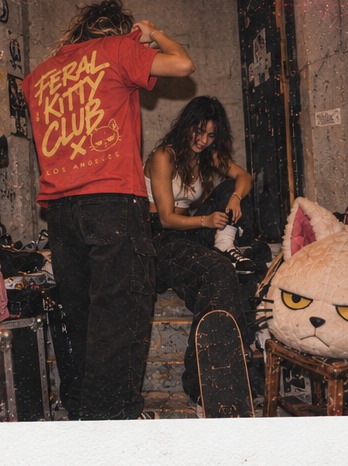 Instant photo of the coral Feral Kitty Club tee, a second model and the mascot head