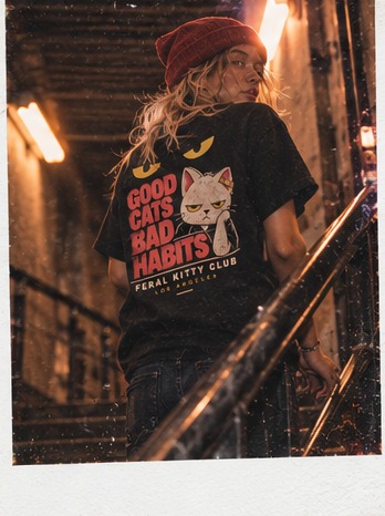 Instant photo of a model in a red beanie and Good Cats Bad Habits tee on a stairwell